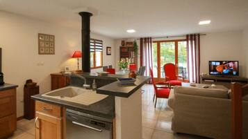 A kitchen with a central island, a dining area with red chairs, a sofa, and a television in the living room.