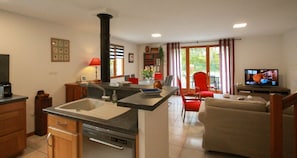 Een keuken met een centraal eiland, een eethoek met rode stoelen, een bank en een televisie in de woonkamer.