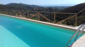 Une piscine dotée d’une terrasse en bois et d’une rambarde en métal, offrant une vue sur un paysage vallonné.