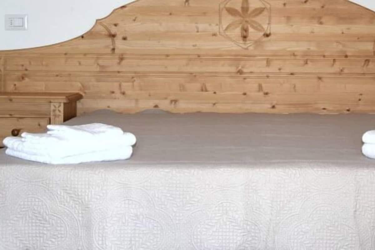 Una cama con cabecera de madera, dos mesitas de noche y toallas dobladas sobre la cama.