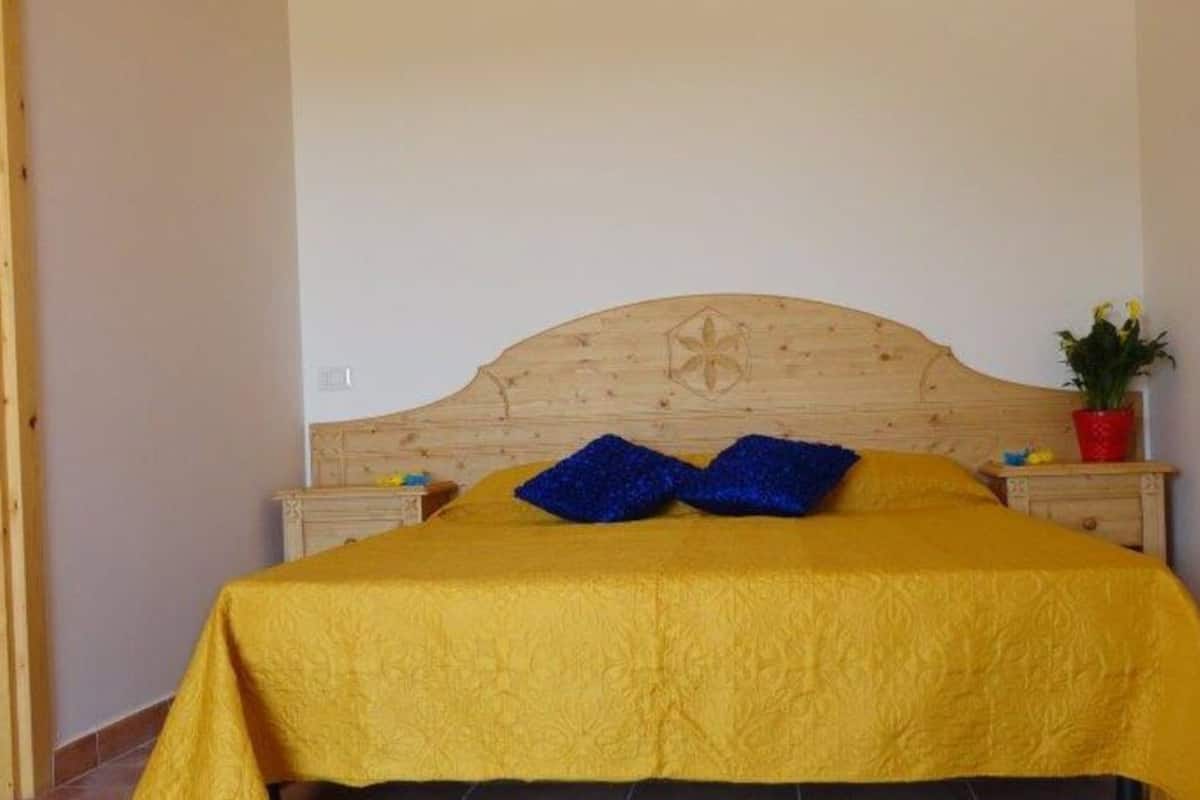 Una cama con cabecera de madera, colcha amarilla y dos almohadas azules.