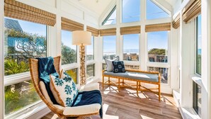 A sunroom with large windows, a wicker chair, a cushioned bench, and a floor lamp.