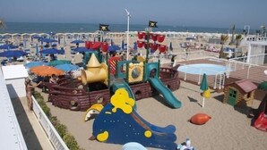 A beachside playground with slides and play structures, a pool, and beach umbrellas. - Hotel Ermeti B&B and Brunch (Riccione)