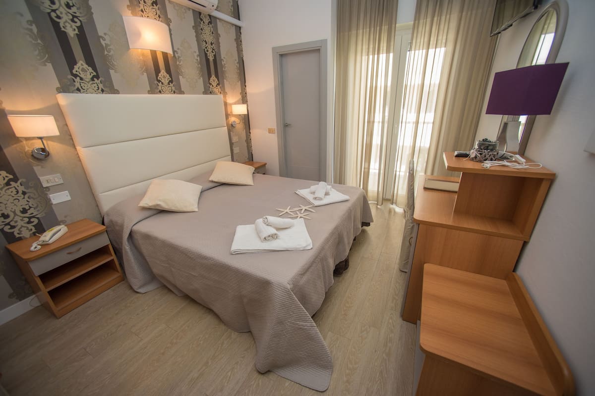 Een netjes ingerichte hotelkamer met een groot bed, bedlampjes, een houten nachtkastje, een spiegel en een klein bureau met lamp.