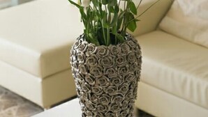 A vase with a textured pattern, filled with white flowers and greenery, placed on a white table in a room with a beige sofa. - Hotel Ermeti B&B and Brunch (Riccione)