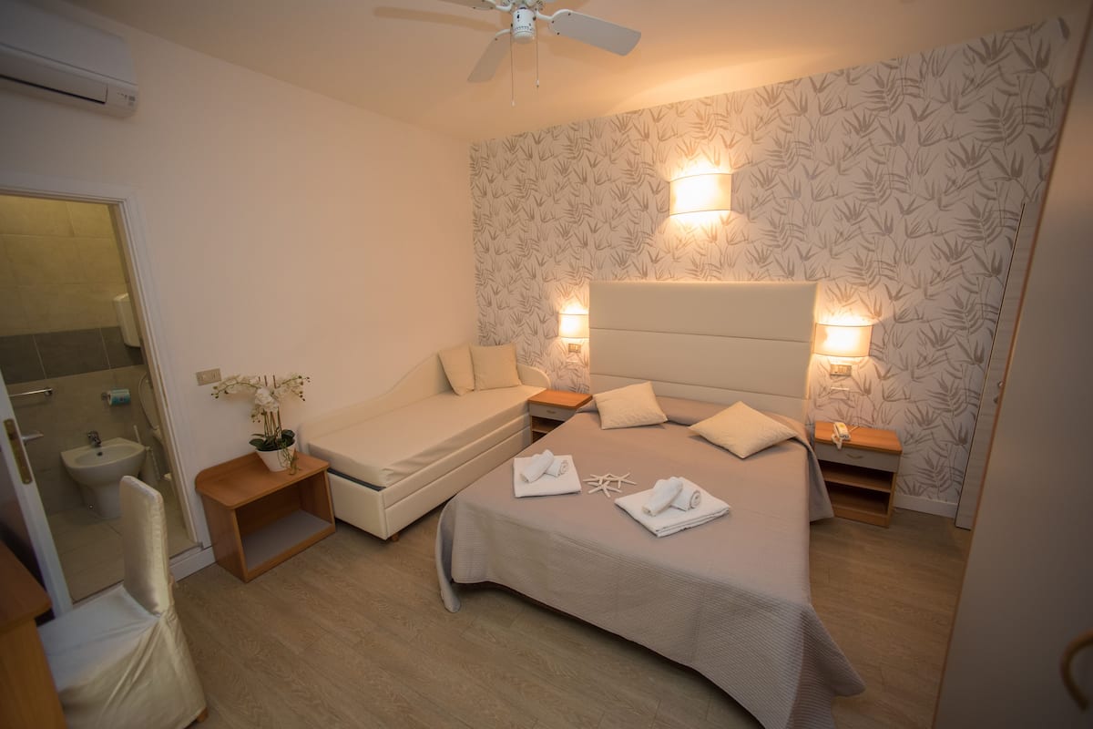 Een hotelkamer met een bed, een slaapbank, een kleine tafel met een plant en een nachtkastje met een lamp.