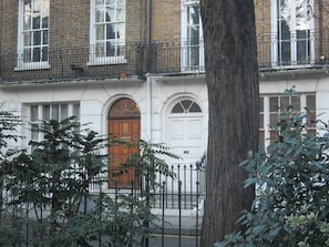 Un bâtiment à deux étages, doté d’une façade blanche, d’une porte d’entrée en bois et d’une clôture en métal noir.