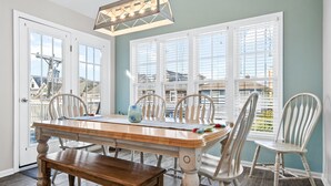 A dining area with a wooden table, four chairs, a bench, and a chandelier. - Beachblock Beauty! Beach & Boards only steps! Bright, huge condo, views galore. (Ocean City)