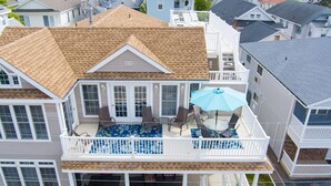 A two-story house with a balcony, a dining area with a table and chairs, and a covered patio with an umbrella. - Beachblock Beauty! Beach & Boards only steps! Bright, huge condo, views galore. (Ocean City)