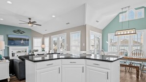 A modern kitchen with white cabinetry, a black countertop, and a large island. There is a ceiling fan, recessed lighting, and a view of the outside through large windows. - Beachblock Beauty! Beach & Boards only steps! Bright, huge condo, views galore. (Ocean City)