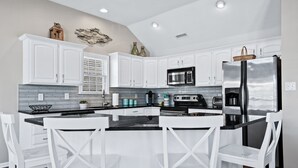 A modern kitchen with white cabinetry, a black countertop, and stainless steel appliances. - Beachblock Beauty! Beach & Boards only steps! Bright, huge condo, views galore. (Ocean City)