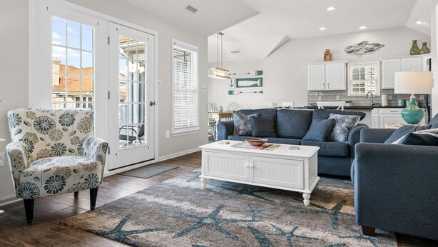 A spacious living room with a large window, a white coffee table, and a blue sofa. - Beachblock Beauty! Beach & Boards only steps! Bright, huge condo, views galore. (Ocean City)