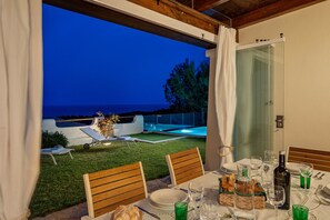An outdoor dining area with a view of the sea, a pool, and a covered patio.