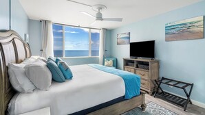 Une chambre avec un grand lit, un ventilateur de plafond, une télévision et une vue sur l’océan.
