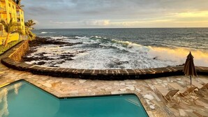 Un espace aménagé au bord de la piscine, avec vue sur l’océan, une terrasse en pierre et un bâtiment doté de balcons.