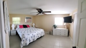 A bedroom with a bed, nightstands, a dresser, a ceiling fan, a TV, and a window with blinds. - Waterfront house in South Ft Myers on Whiskey creek (Fort Myers)