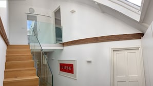 Ein modernes Interieur mit einer Holztreppe, einem Glastrennwerk und einer weißen Tür. An der Wand ist ein rotes Schild angebracht.
