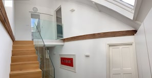 Un interior moderno con una escalera de madera, barandilla de vidrio, una puerta blanca y un letrero rojo en la pared.