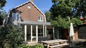 Ein zweistöckiges Haus mit einer Terrasse, einem Holztisch und einem Grill.