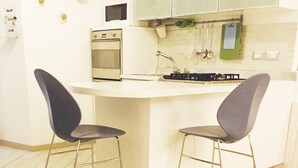 Une petite cuisine équipée d’une cuisinière, d’un four à micro-ondes et d’ustensiles de cuisine suspendus. On y trouve deux chaises et une table avec une théière et des tasses.