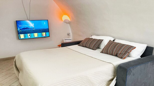 Une chambre à coucher avec un lit, des oreillers, un téléviseur fixé au mur et une lampe fixée au mur.