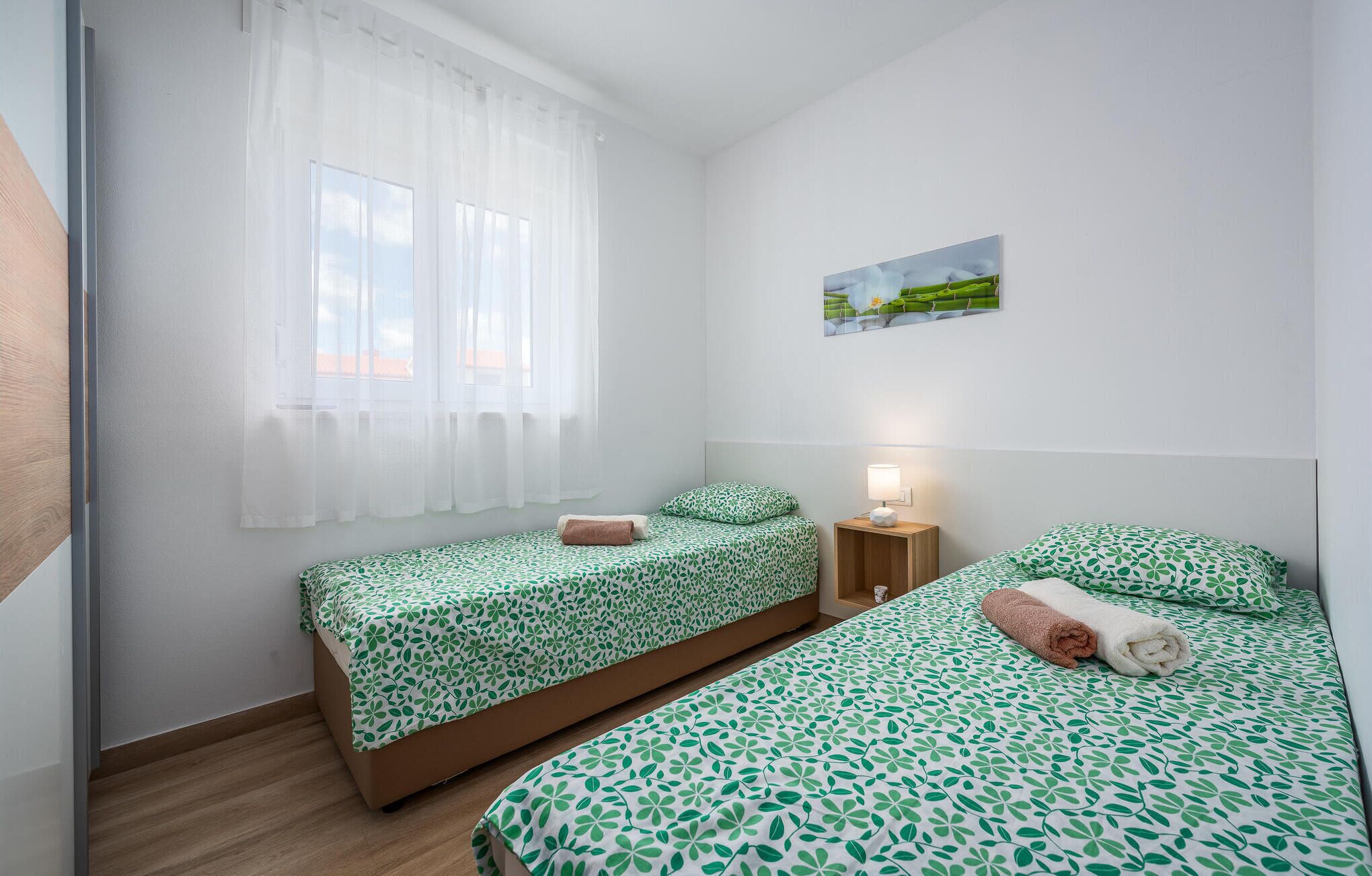A bedroom with two single beds, a nightstand, a lamp, and a window with sheer curtains.