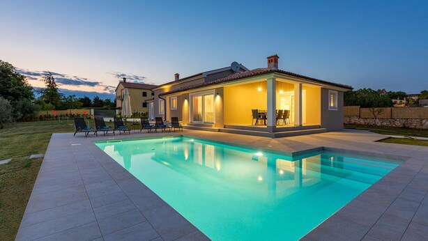 Ett modernt hus med en swimmingpool, utomhusmöbler och en väl upplyst uteplats.