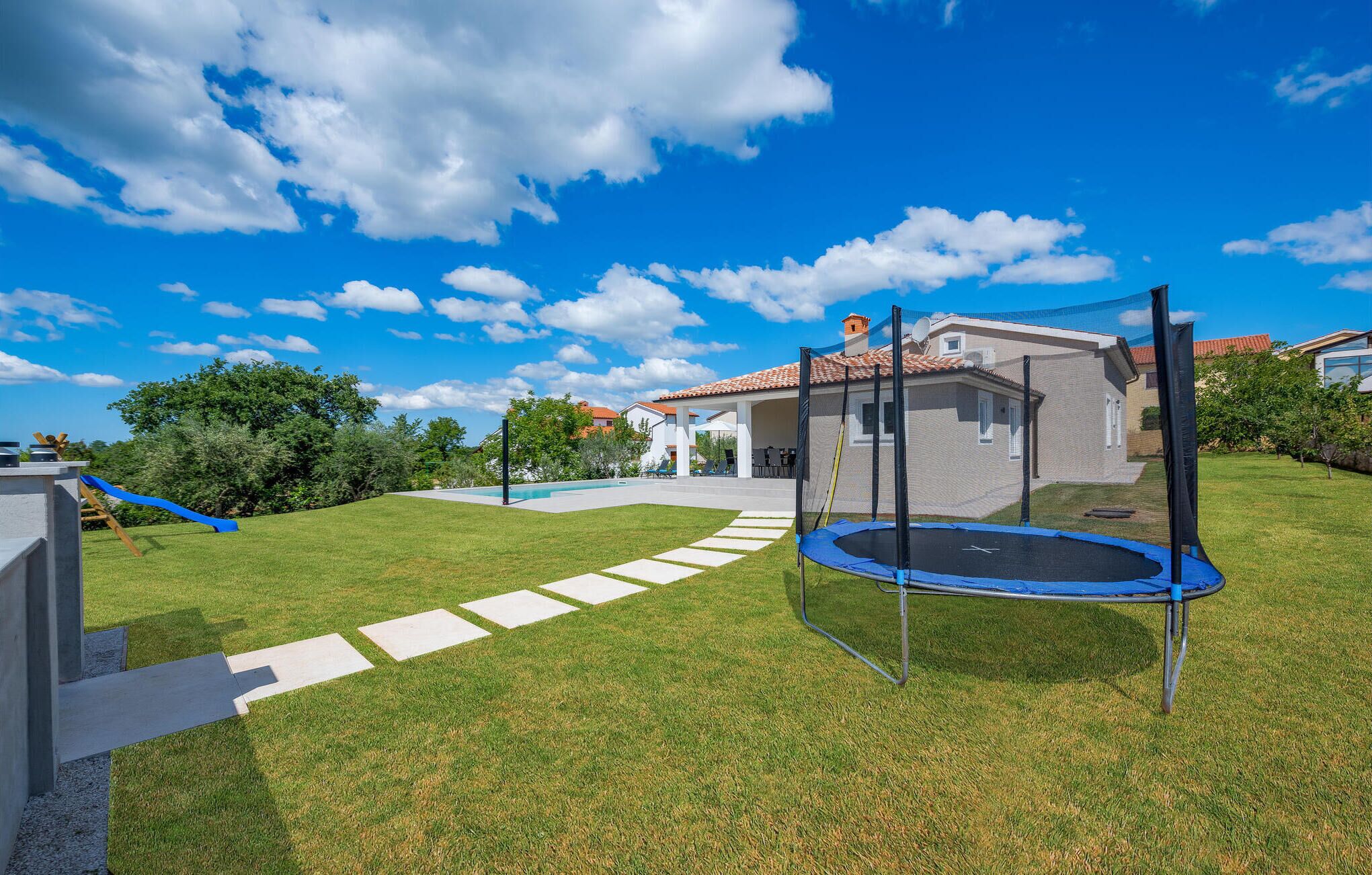 Ein Garten mit Trampolin, Terrasse und einem Haus mit Ziegeldach.