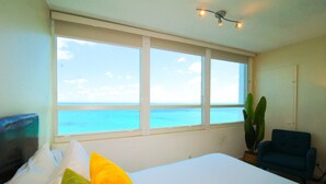 A bedroom with a large window, a bed with pillows, a chair, and a plant. - Castle 1733 Oceanfront Studio with pool, beach access, free parking, gym, tennis and more! (Miami Beach)