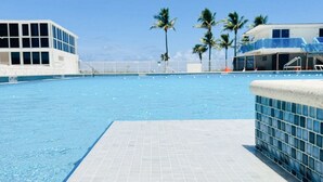 A swimming pool with a tiled deck, palm trees, and buildings in the background. - Castle 1733 Oceanfront Studio with pool, beach access, free parking, gym, tennis and more! (Miami Beach)