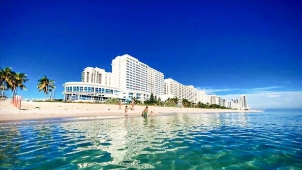 A beachfront hotel with multiple high-rise buildings, clear blue water, and palm trees. - Castle 1733 Oceanfront Studio with pool, beach access, free parking, gym, tennis and more! (Miami Beach)