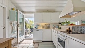 A compact kitchen with white cabinets, a built-in oven, and a sink. There is a small dining area with a bench and a table. - 4 bedroom amazing home in Hornbæk (Hornbæk)