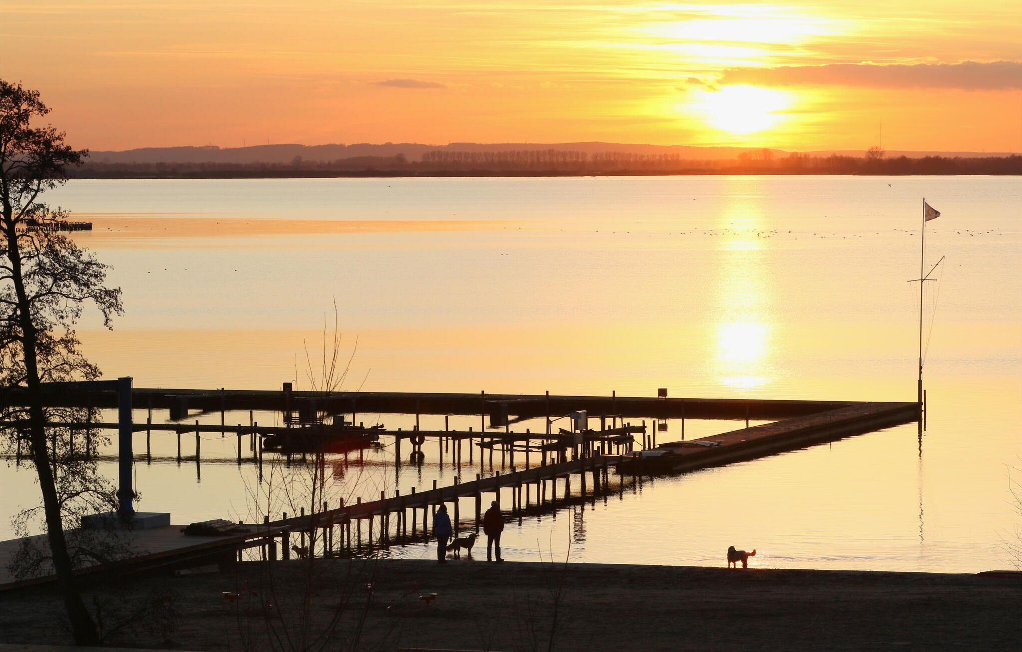 A sunset over a calm lake with a wooden pier extending into the water.