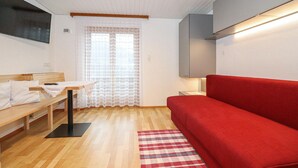 Ein modernes Wohnzimmer mit einem roten Sofa, einer Holzbank, einem kleinen Tisch und einem gemusterten Teppich.