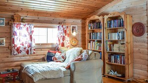 A cozy cabin-style room with a bed, a bookshelf, and a window with curtains.
