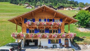 Un chalet en bois doté d’un balcon orné de jardinières suspendues, d’un garage et d’un chemin de pierre menant à l’entrée.