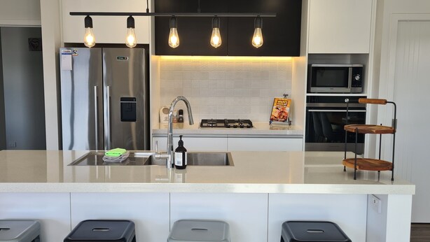 Een moderne keuken met een centraal eiland, roestvrijstalen apparatuur en hangende lampen.