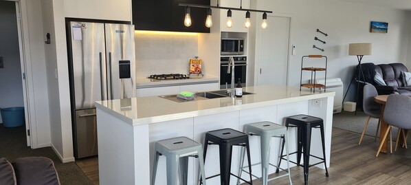 A modern kitchen with a central island, bar stools, a microwave, oven, and a gas stove.