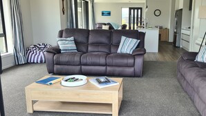 Een moderne woonkamer met een donkerbruine leren bank, een houten bijzettafeltje met boeken en een schaal, en een gestreept loungestoel.