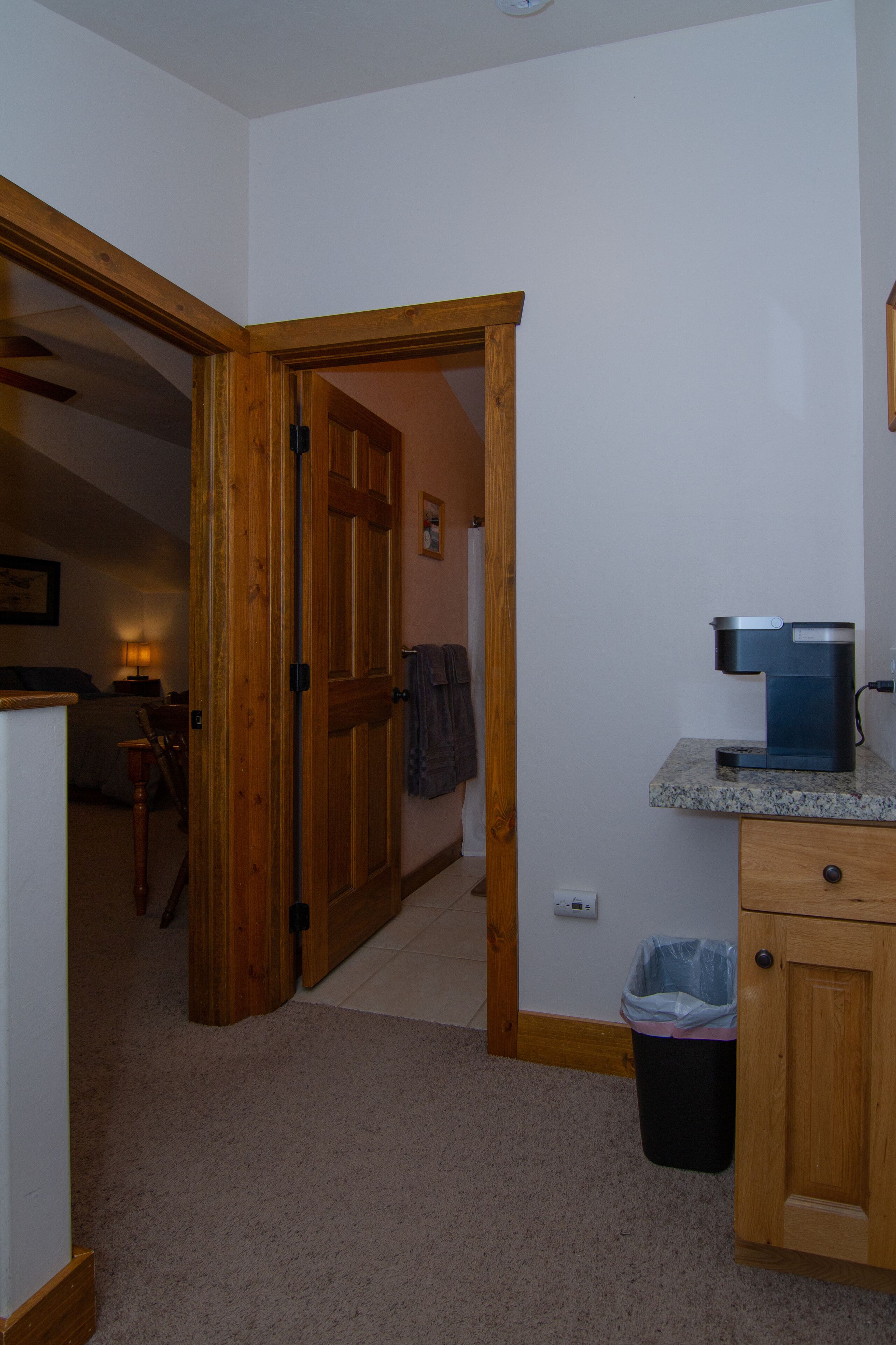 A kitchen with a coffee maker, wooden cabinets, and a trash can.
