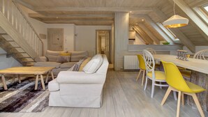 Un loft spacieux avec un plafond haut, un coin repas avec des chaises jaunes, un ensemble de canapés et un escalier.