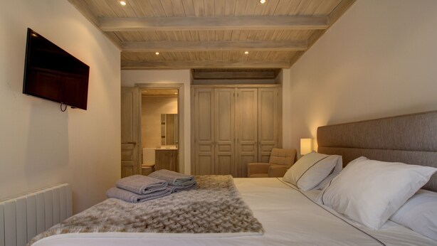 Une chambre dotée d’un grand lit, d’un téléviseur à écran plat fixé au mur, d’un plafond en bois et d’un dressing avec portes coulissantes.