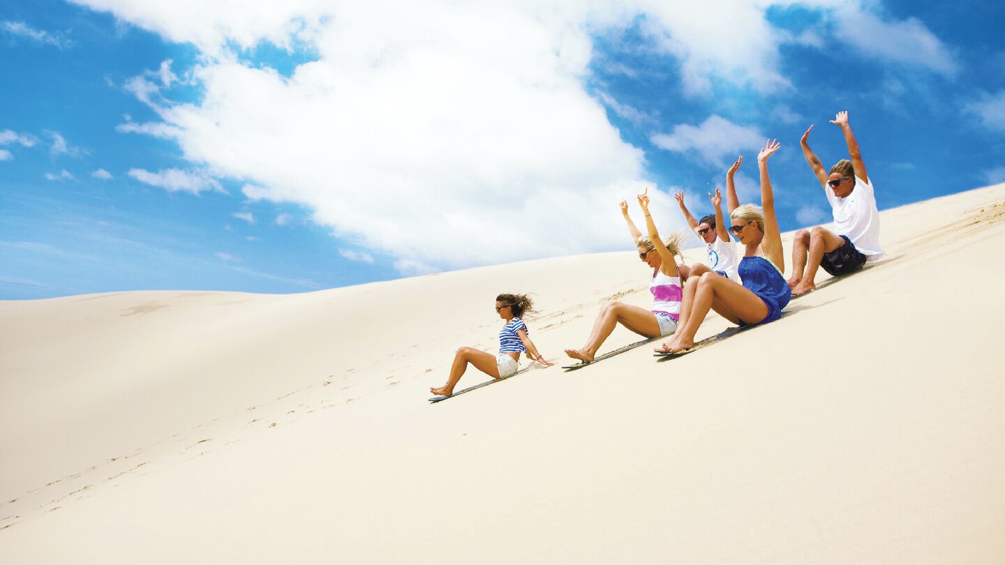 Un groupe de personnes assises sur une dune de sable, avec un ciel dégagé en arrière-plan.