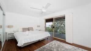 A bedroom with a bed, a ceiling fan, a nightstand, a lamp, and a view of the outdoors through a sliding door.