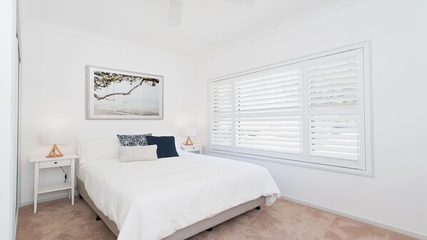 A bedroom with a bed, a nightstand, a lamp, a picture on the wall, and a window with blinds.