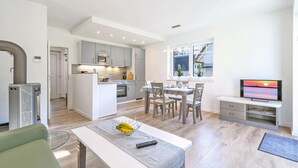 Et moderne køkken med en central ø, spiseområde med stole, et fjernsyn og et lille bord med en fjernbetjening.