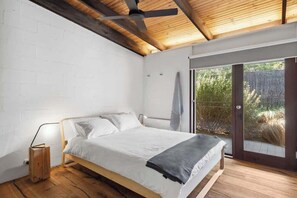 A bedroom with a bed, a ceiling fan, a wooden floor, and a sliding glass door to the outside.