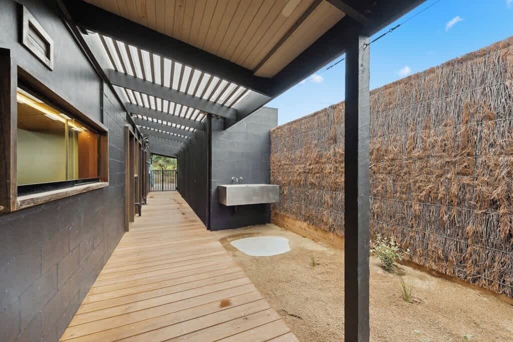 A modern outdoor bathroom with a wooden deck, a large sink, and a wall covered with straw.