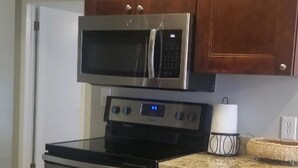 Une cuisine dotée de meubles en bois, d’un four à micro-ondes en acier inoxydable, d’une cuisinière et d’un plan de travail sur lequel se trouve un panier.