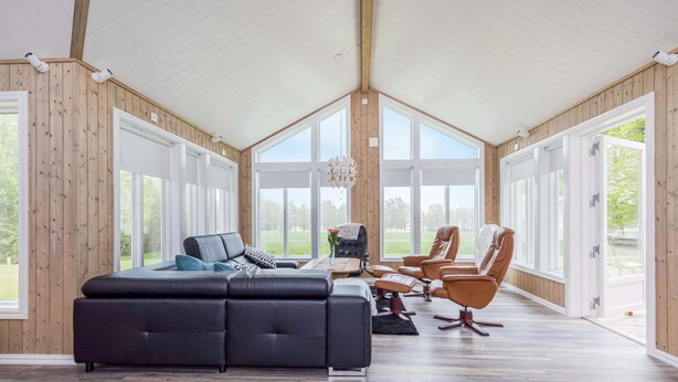 A spacious room with a large black sectional sofa, a dining table with chairs, and large windows offering a view of the outdoors.